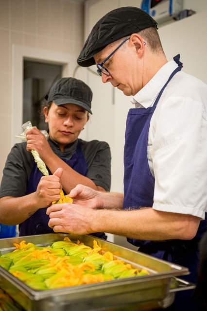 Deux cuisiniers du restaurant La Table d’Elka préparant des fleurs de courgette farcies à l’aide d’une poche à douille en cuisine.