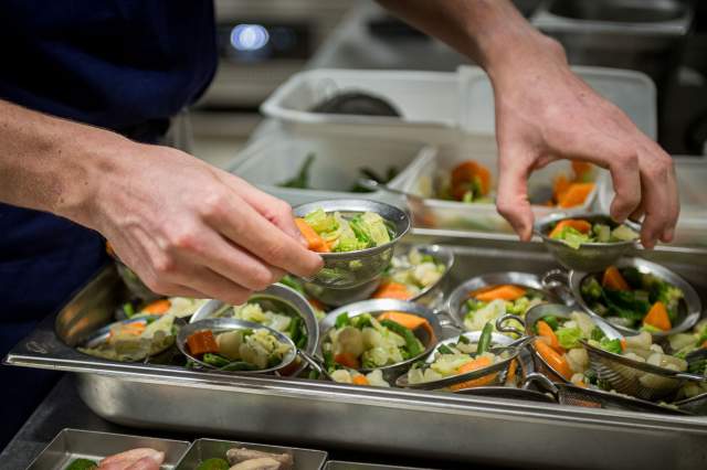 Préparation de plusieurs assiettes de légumes frais en cuisine au restaurant La Table d’Elka, avant le service.
