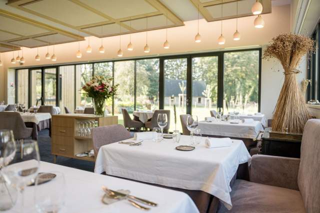 Salle lumineuse du restaurant La Table d’Elka, avec tables dressées, grandes baies vitrées et vue sur le parc arboré.