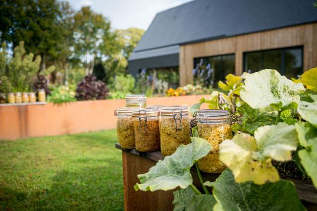 Pots de conserves maison disposés dans le jardin du restaurant La Table d’Elka, devant la façade en bois et les massifs de plantes.