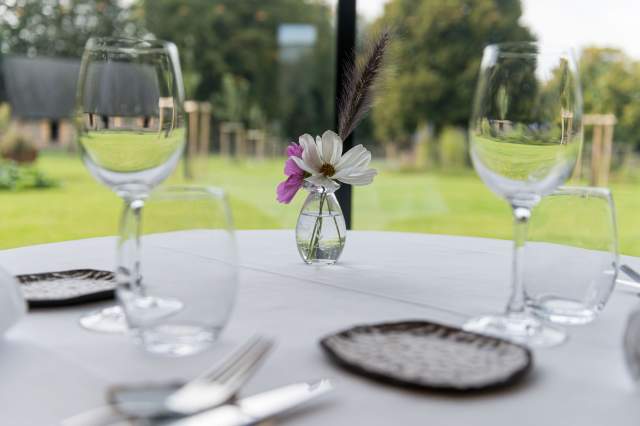 Table élégamment dressée au restaurant La Table d’Elka, avec verres à vin, couverts et petit vase de fleurs face au jardin.