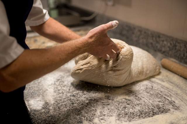 Préparation d’une pâte à pain faite maison au restaurant La Table d’Elka, un chef pétrissant la pâte sur un plan de travail fariné.