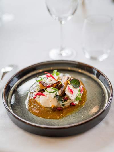 Entrée gastronomique du restaurant La Table d’Elka, composée de légumes, de sauce et d’herbes fraîches dans une assiette creuse.