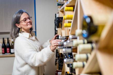 Femme sélectionnant une bouteille dans la cave à vins du restaurant La Table d’Elka, devant un mur de rangements en bois.