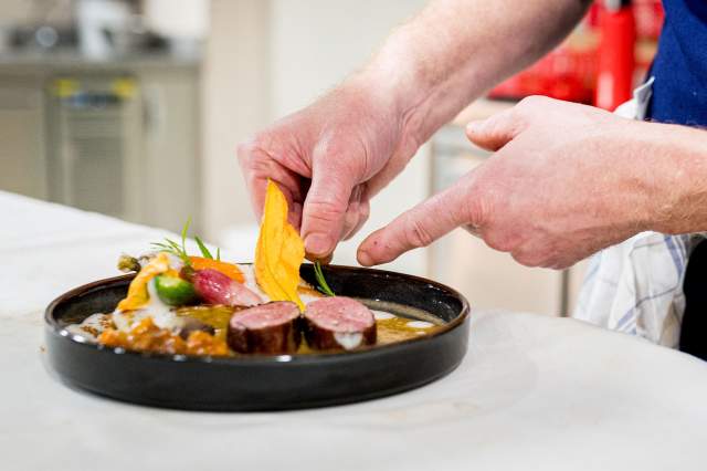 Dressage d’un plat gastronomique au restaurant La Table d’Elka, un chef disposant une fleur comestible sur une assiette de viande et de légumes.