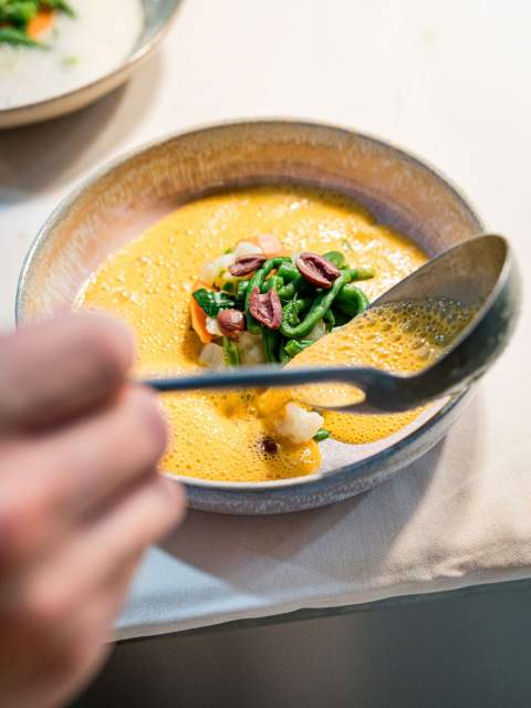 Dressage d’un plat de poisson nappé d’une sauce orangée au restaurant La Table d’Elka, avec ajout de légumes et herbes fraîches.