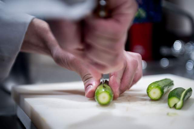 Préparation en cuisine au restaurant La Table d’Elka, gros plan sur la coupe d’un légume vert avec un couteau sur une planche.