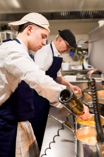 Cuisiniers du restaurant La Table d’Elka en pleine préparation en cuisine, ajoutant des ingrédients dans une poêle chaude.