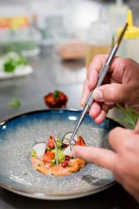 Dressage minutieux d’une assiette gastronomique au restaurant La Table d’Elka, avec des pinces de cuisine et des ingrédients frais.