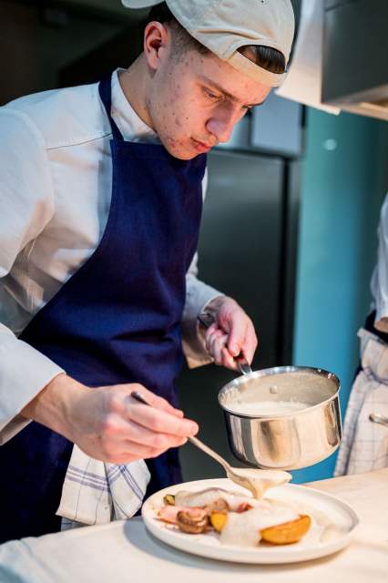 Cuisinier du restaurant La Table d’Elka versant une sauce dans une assiette à l’aide d’une louche en cuisine.