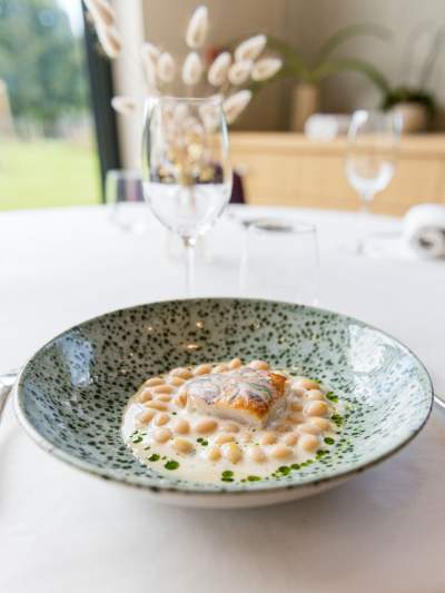 Plat gastronomique du restaurant La Table d’Elka, composé d’un poisson et de haricots blancs servis dans une sauce crémeuse.