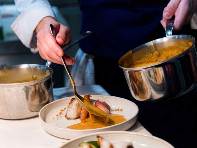 Dressage d’un plat de viande avec une sauce orangée au restaurant La Table d’Elka, un chef versant la sauce à la cuillère.