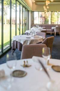 Tables dressées dans la salle du restaurant La Table d’Elka, avec vue panoramique sur le jardin grâce à de grandes baies vitrées.